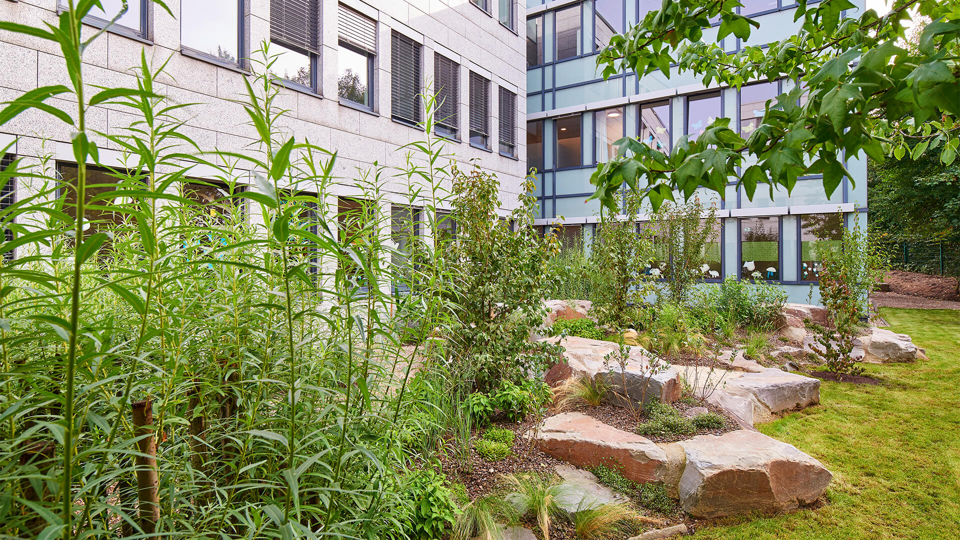 Garten der Kindertagesstätte mit Wiese, Natursteinen, Beet, Bäumen und vielen Sträuchern