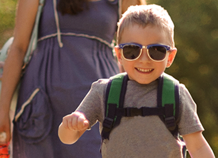 Fröhliches Kind auf Ausflug mit Sonnenbrille und Mutter bei Sonnenschein