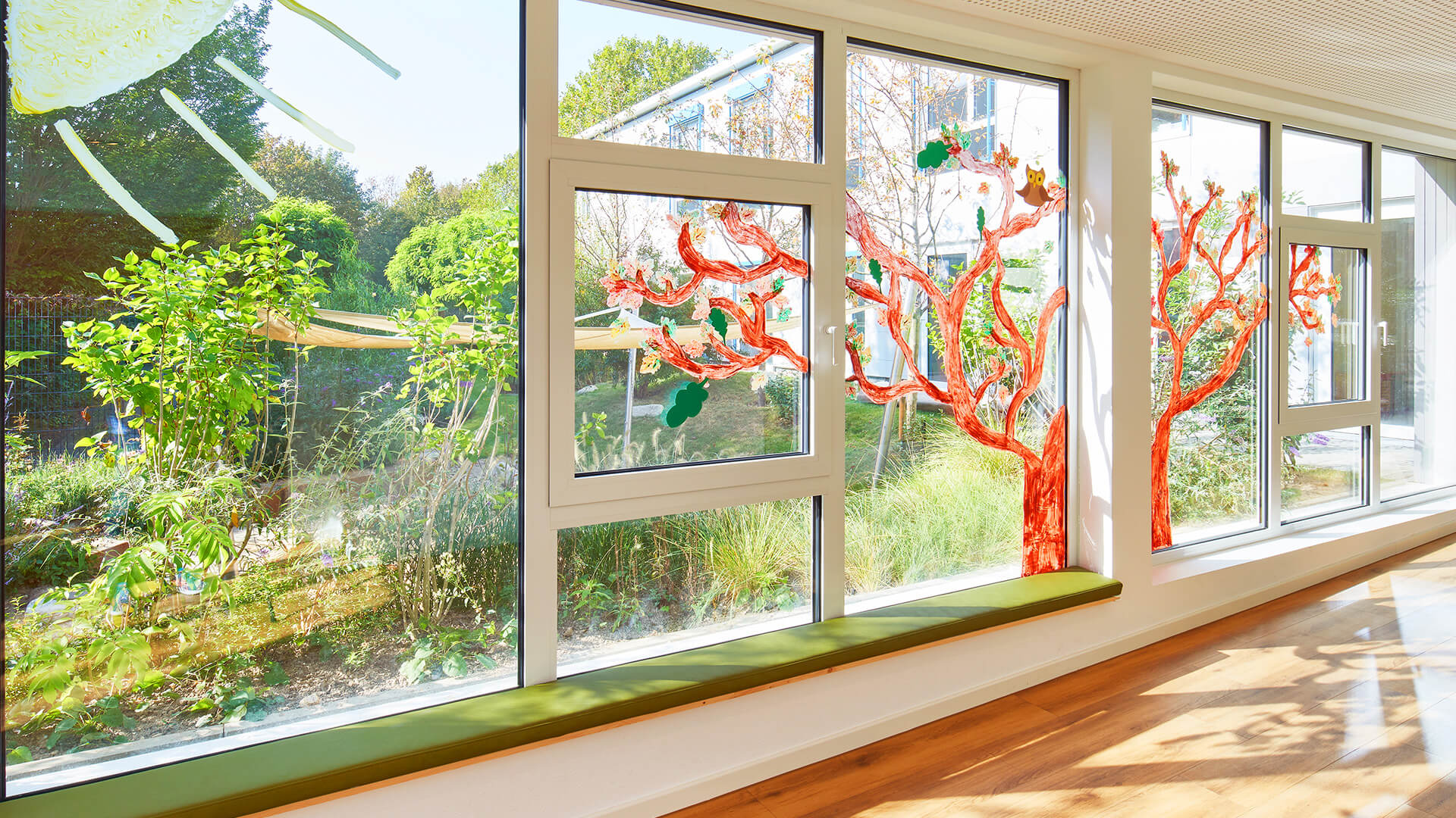 Große, von den Kindern bemalte Fenster mit Sonne, Baum und einer Eule. Blick auf den großzügigen Garten.
